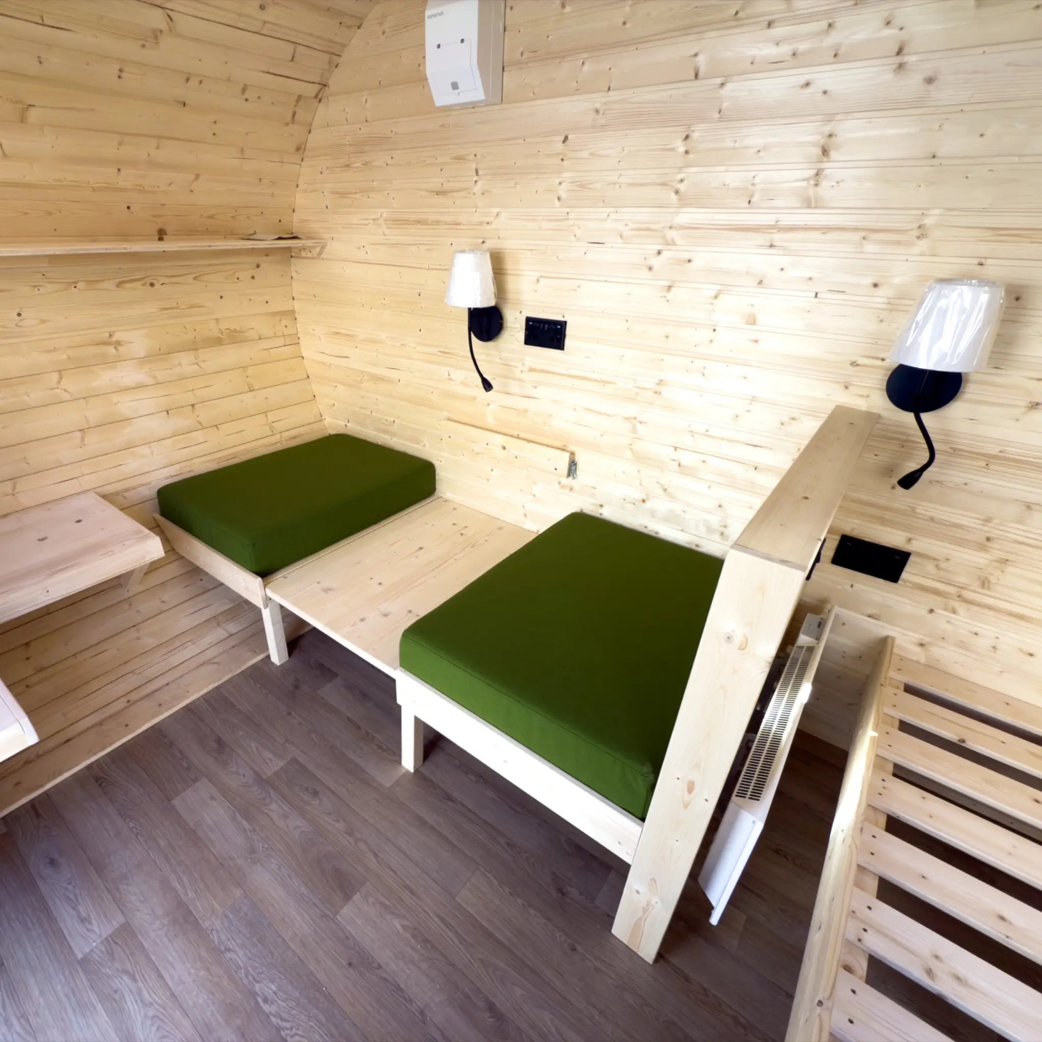 Interior of Grotto glamping pod with convertible bed seating, green cushions and wooden finish