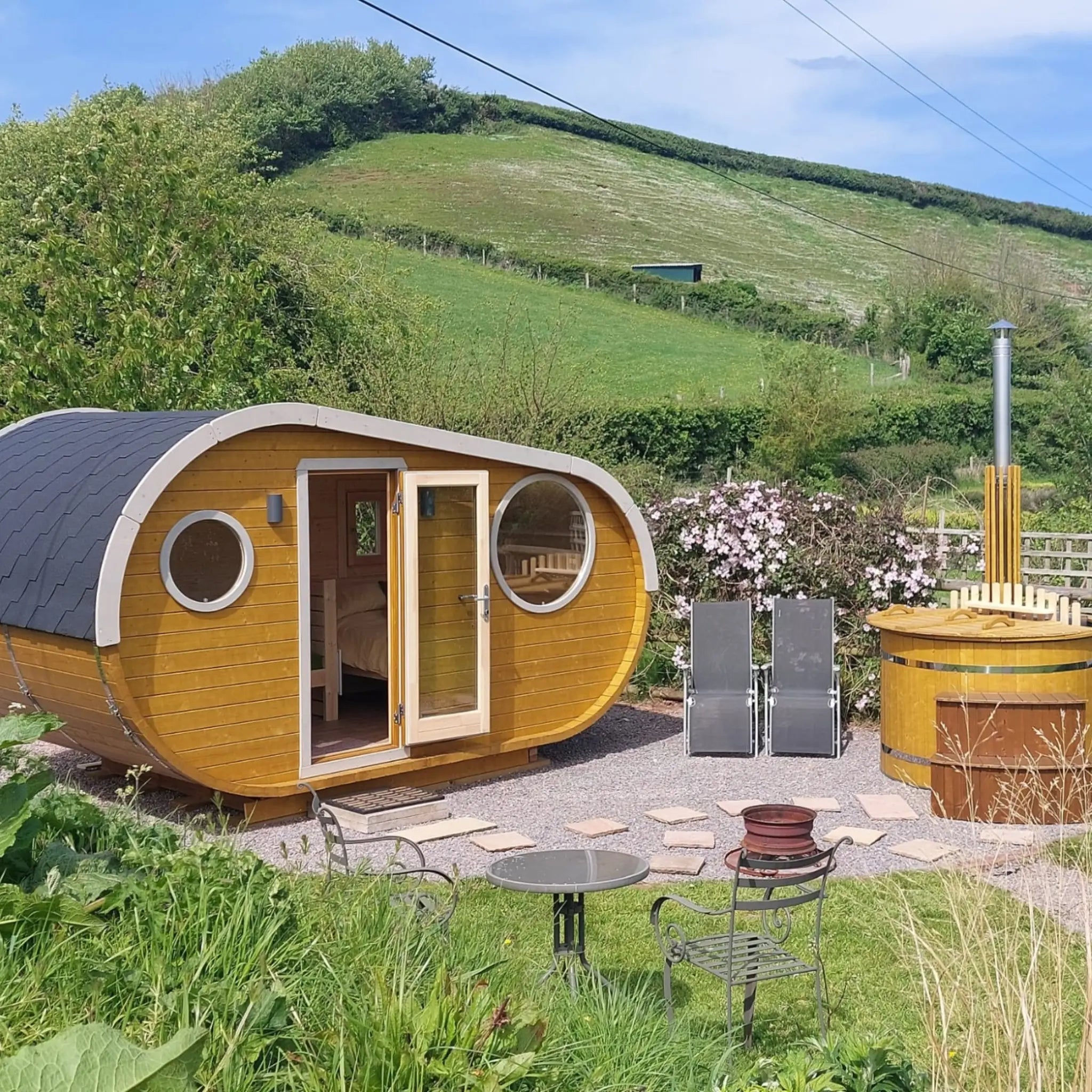 Luxury 3 person glamping pod exterior with wood-fired hot tub in countryside setting