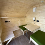 Interior layout of Grotto glamping pod showing convertible seating area, table and natural timber walls