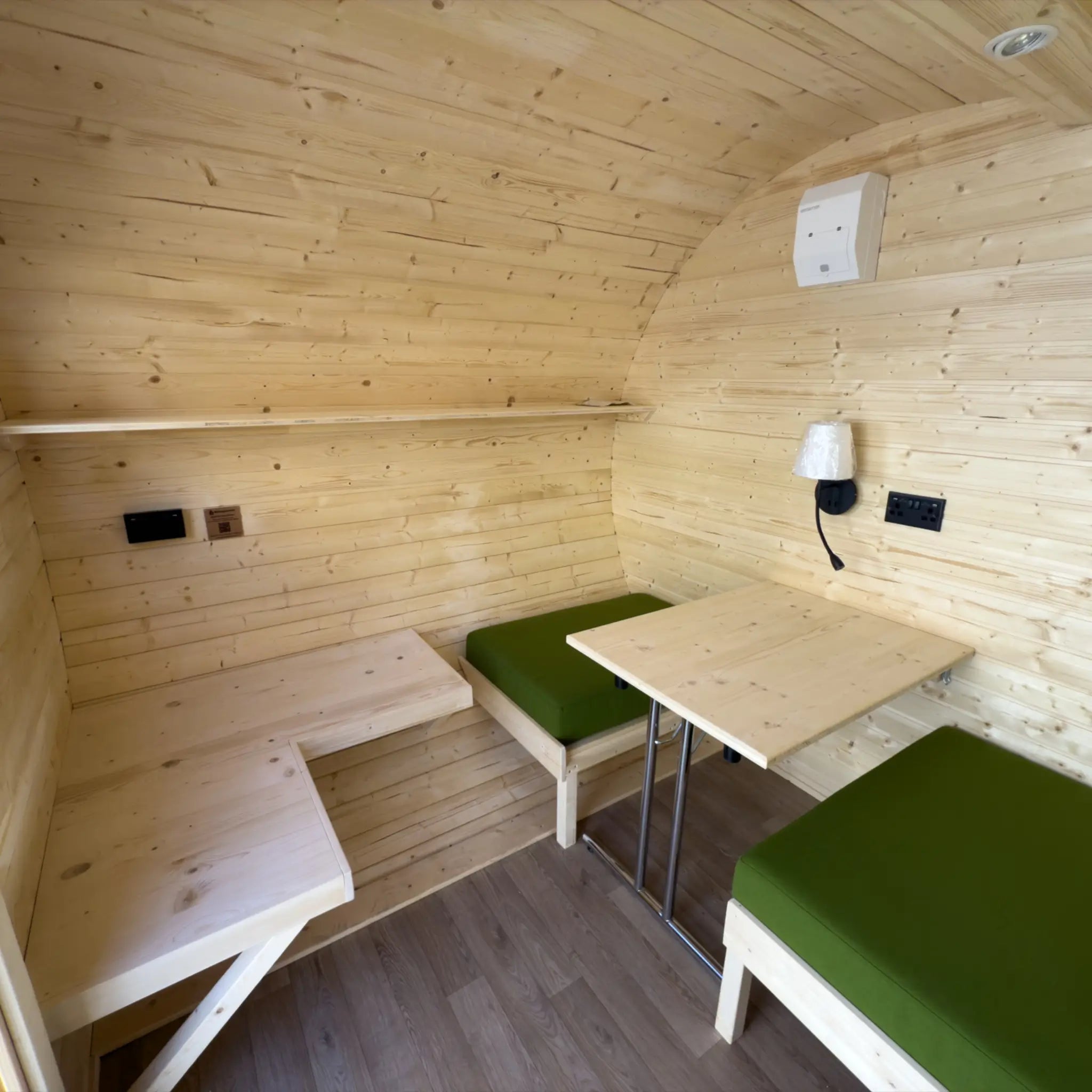 Interior layout of Grotto glamping pod showing convertible seating area, table and natural timber walls