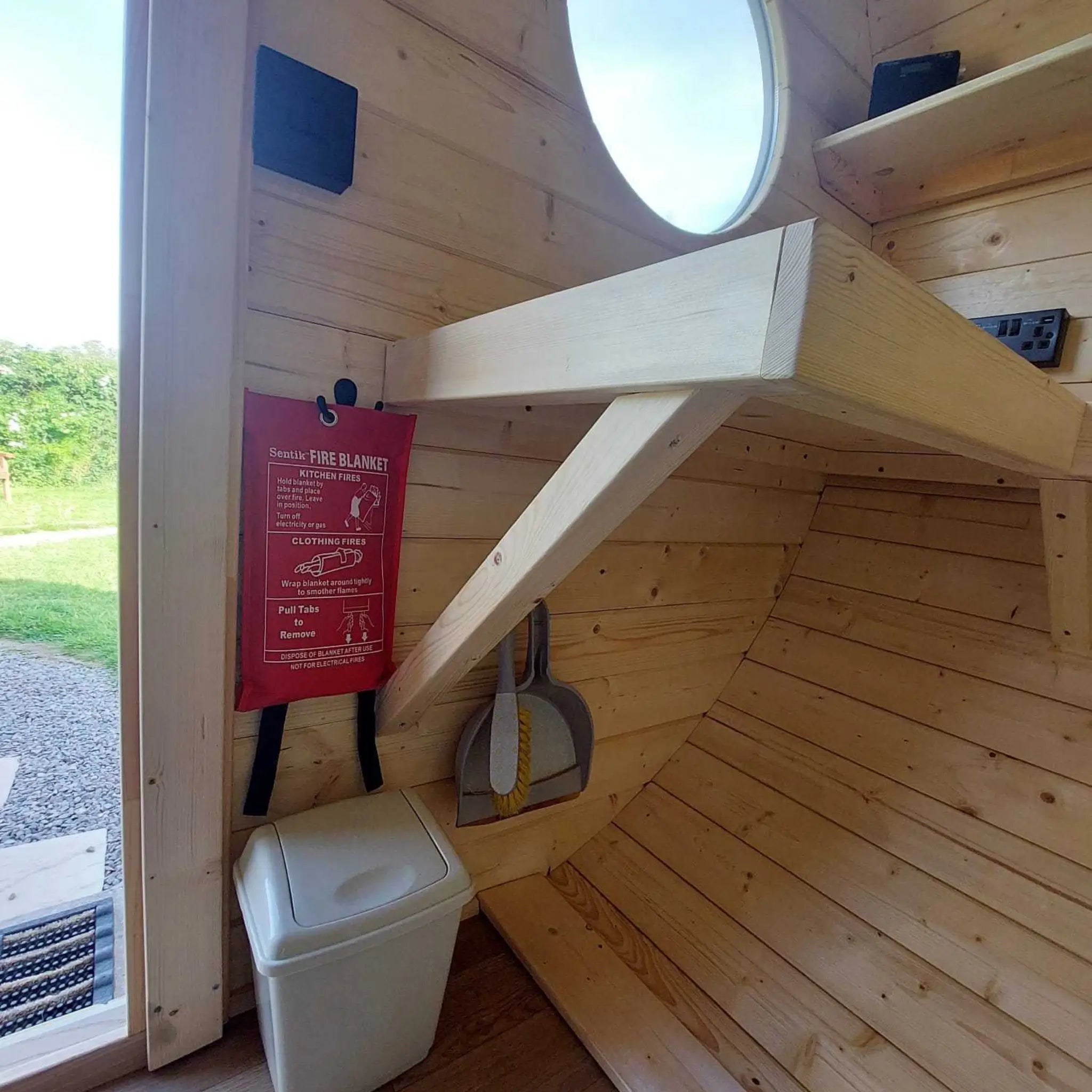 Wall-mounted storage table with fire blanket and waste bin inside a glamping pod