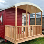 Front exterior view of The Hawthorne luxury shepherds hut with covered timber porch, curved roof and red cladding.