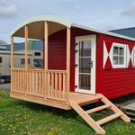 Exterior side profile of The Hawthorne luxury shepherds hut with red wooden cladding and decorative window shutters.