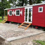 Angled exterior view of The Hawthorne 2 berth shepherds hut with side steps, red timber cladding and countryside setting.