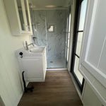 Modern shepherds hut bathroom interior with walk-in shower, vanity sink, marble-effect wall panels and wood flooring.