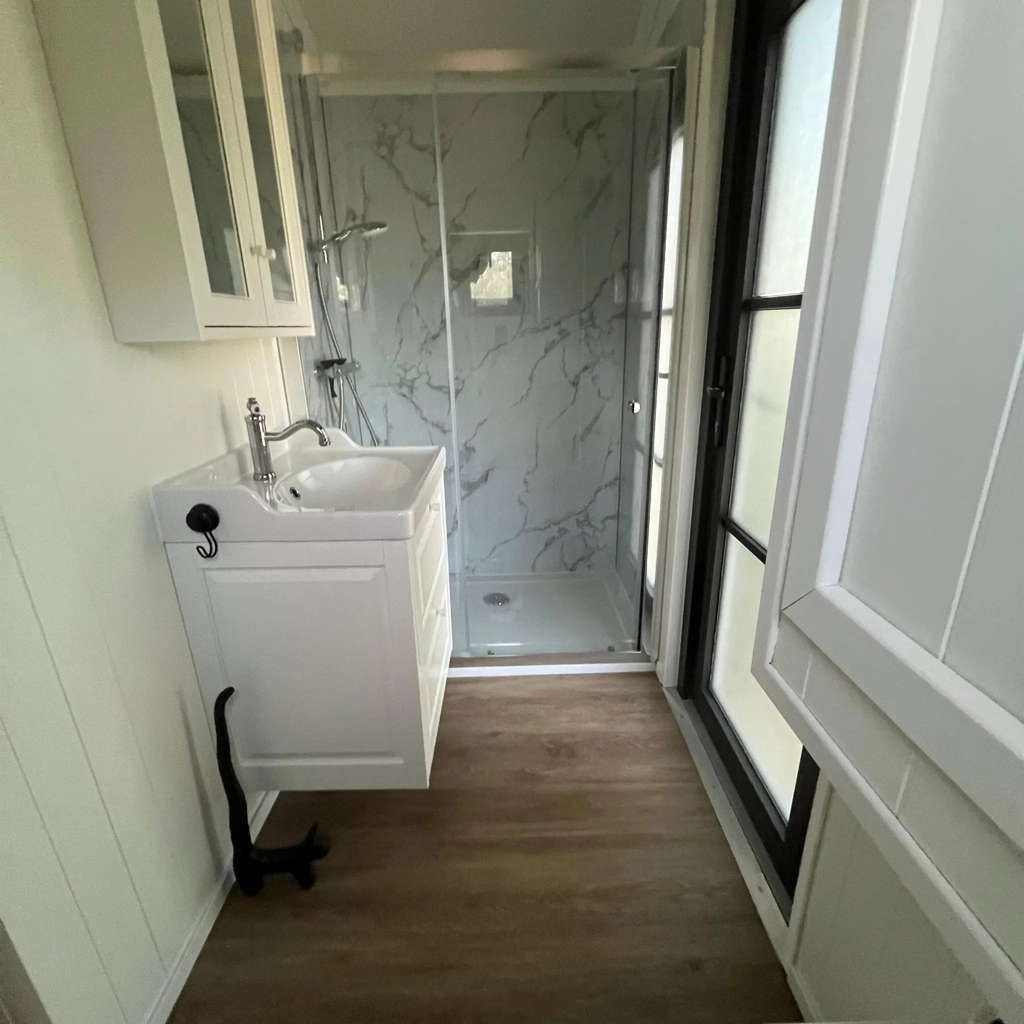Modern shepherds hut bathroom interior with walk-in shower, vanity sink, marble-effect wall panels and wood flooring.