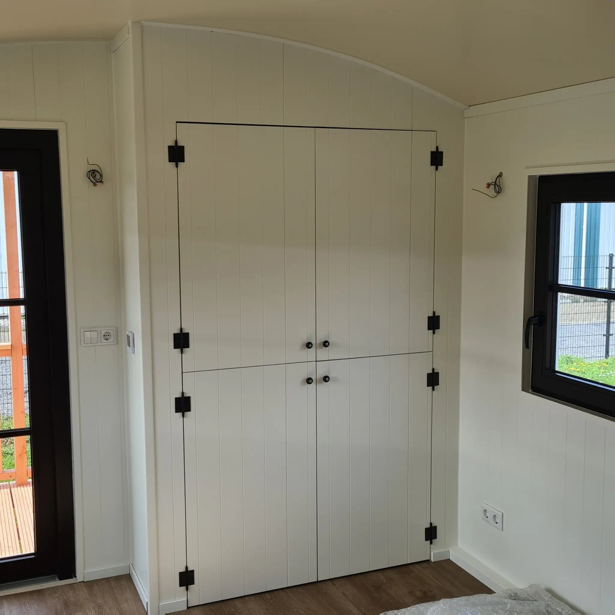 Closed bathroom storage doors inside The Hawthorne shepherds hut with custom cabinetry and modern black hardware.