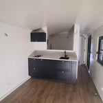 Open-plan kitchenette inside The Hawthorne shepherds hut with modern black cabinets, sink and luxury finishes.