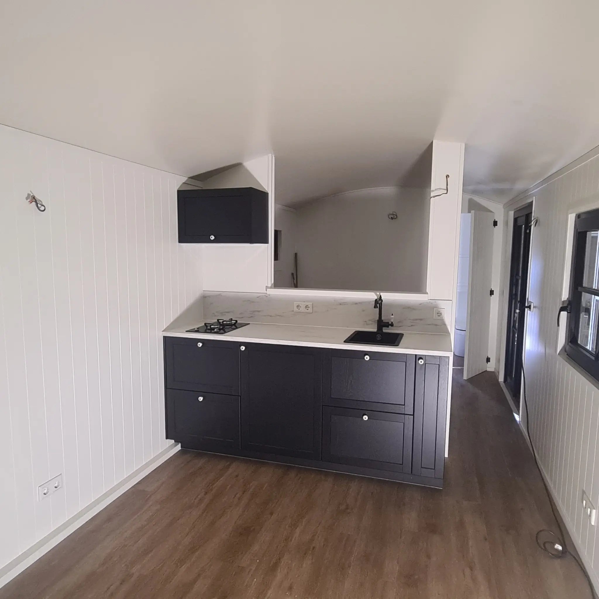 Open-plan kitchenette inside The Hawthorne shepherds hut with modern black cabinets, sink and luxury finishes.