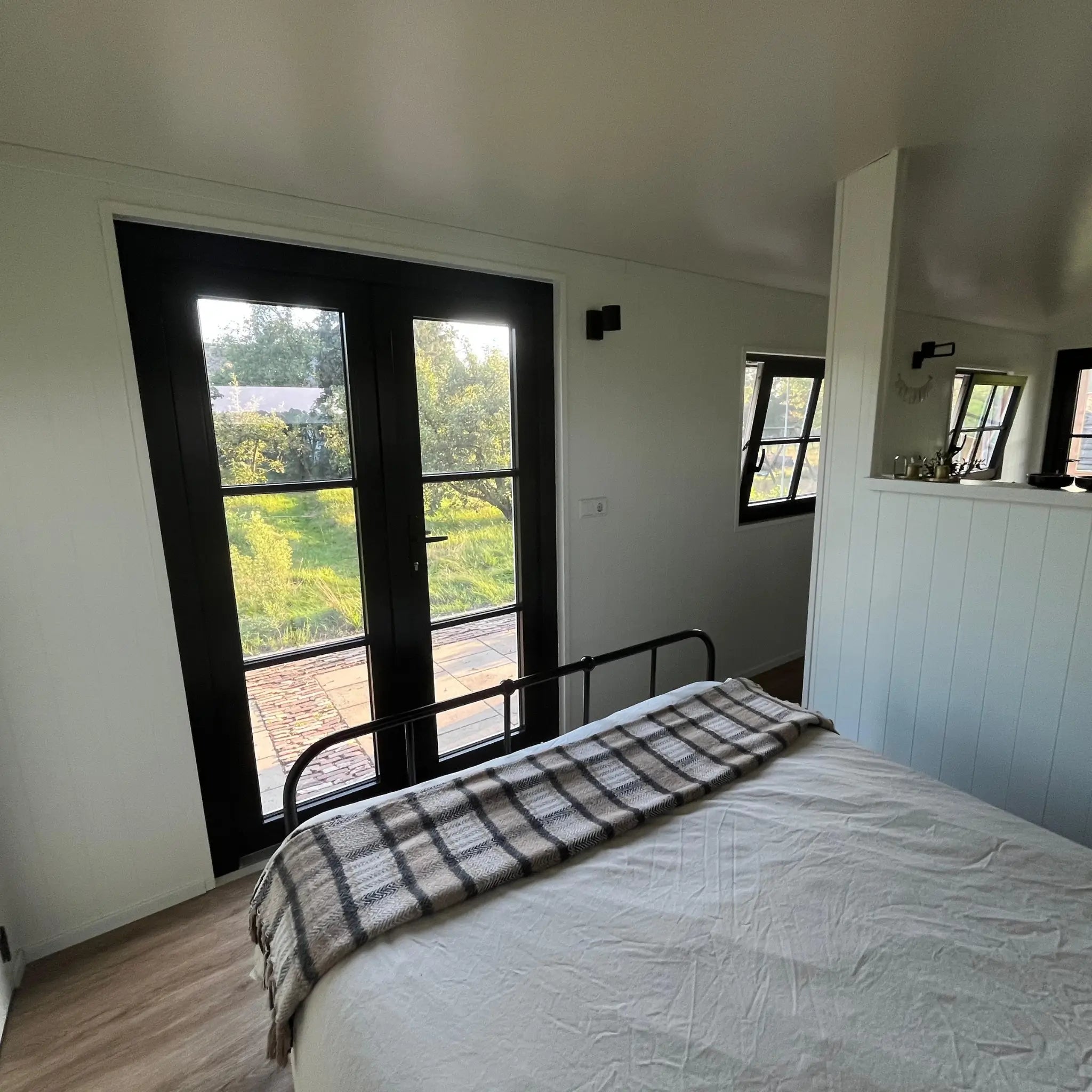 Sleeping area inside The Hawthorne luxury shepherds hut with double bed, black framed doors and countryside views.