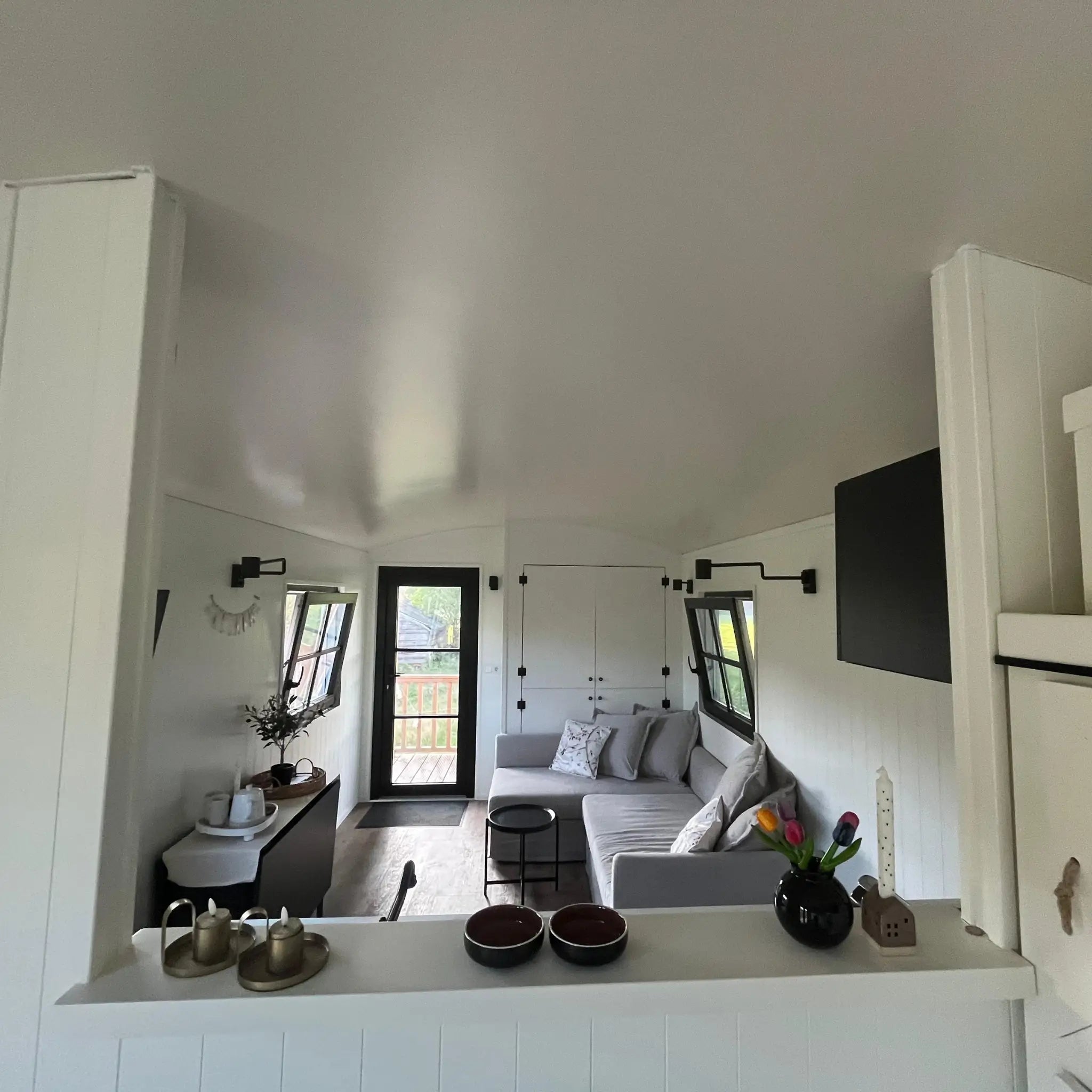 View of living area from decorative cabinet inside The Hawthorne shepherds hut with lounge seating and open-plan layout.