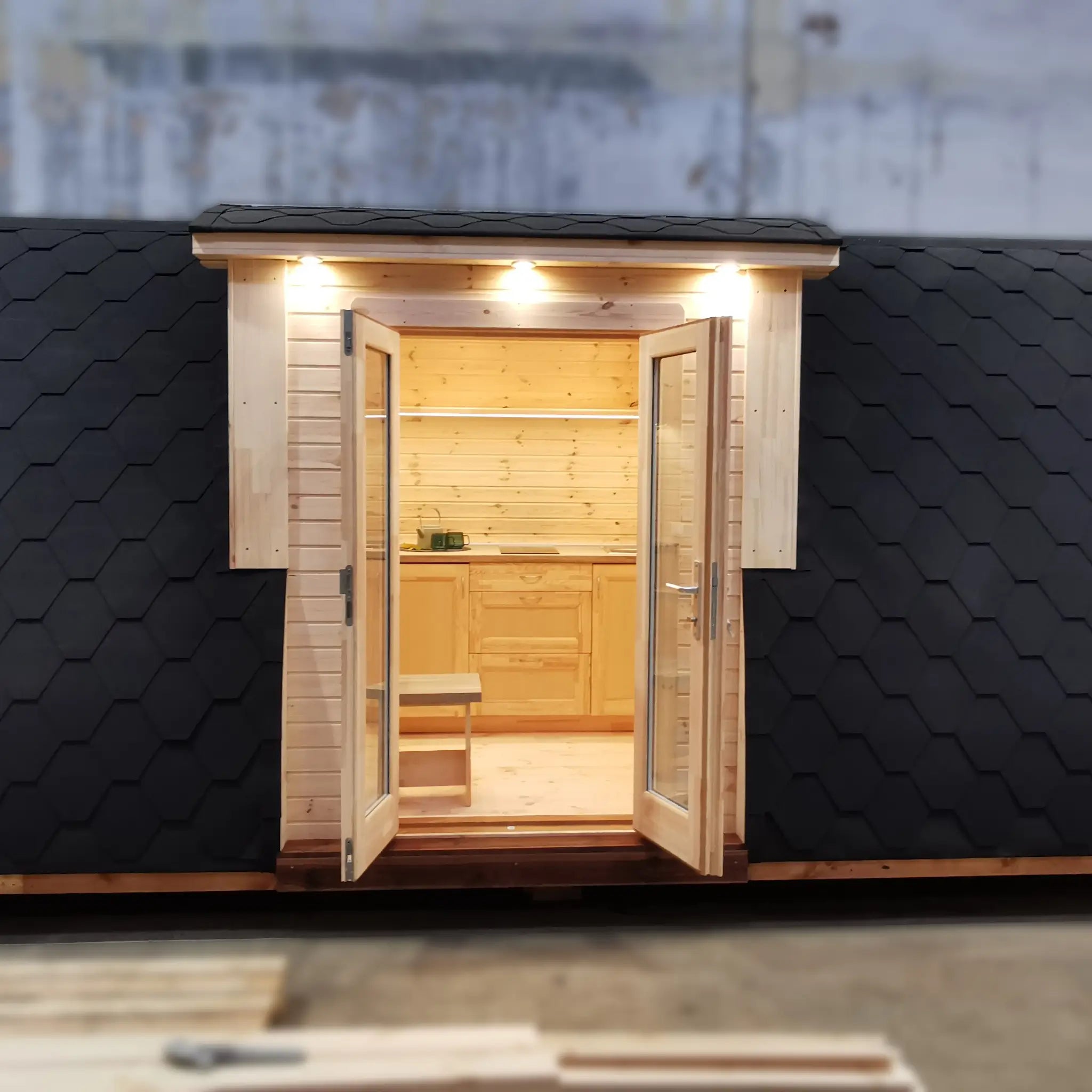Front exterior close-up showing curved roof, timber cladding, and illuminated entrance of the Hearthwood Pod 5 Person Glamping Pod with disabled access