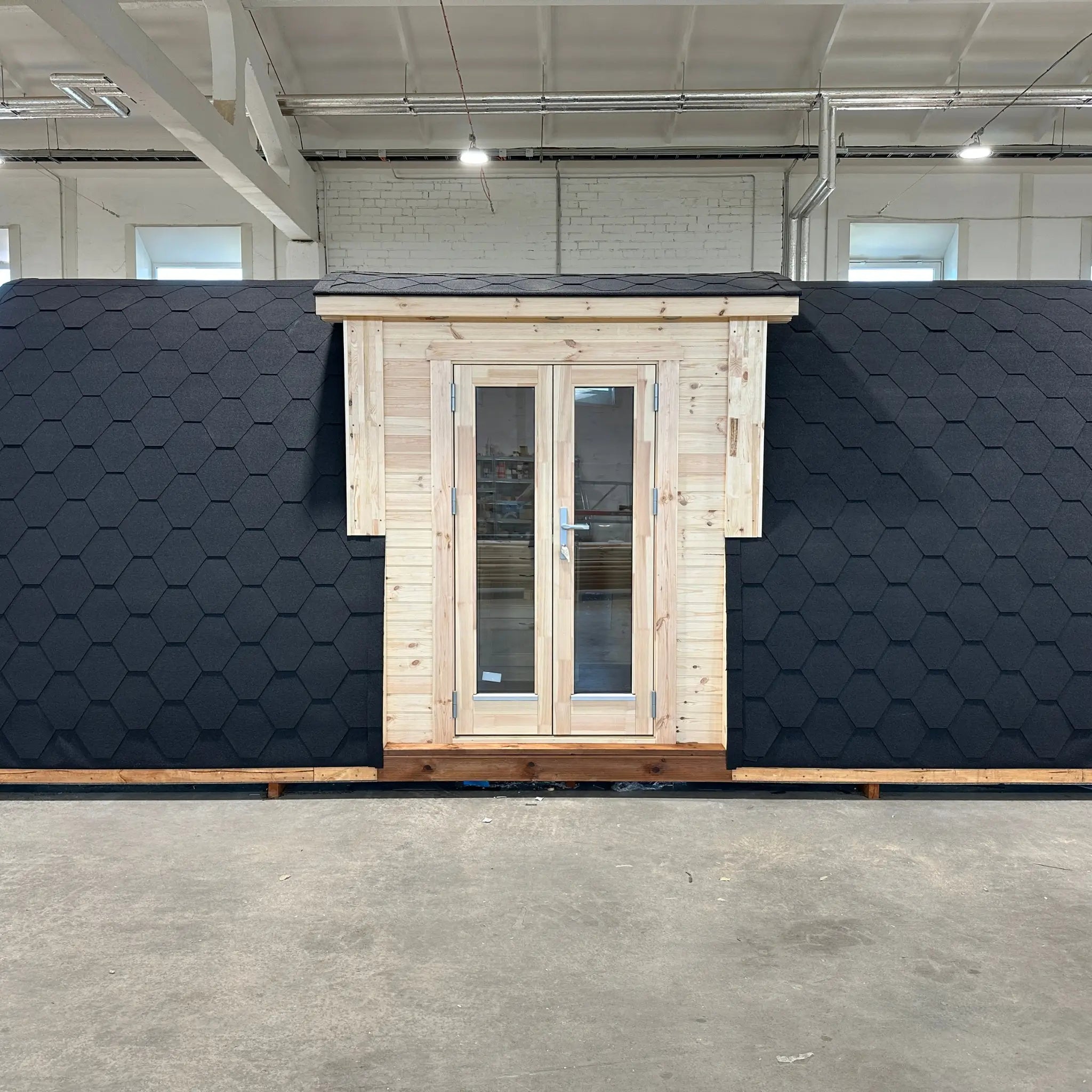 Front exterior view of the Hearthwood luxury 2–4 person glamping pod with timber entrance and black shingle curved roof