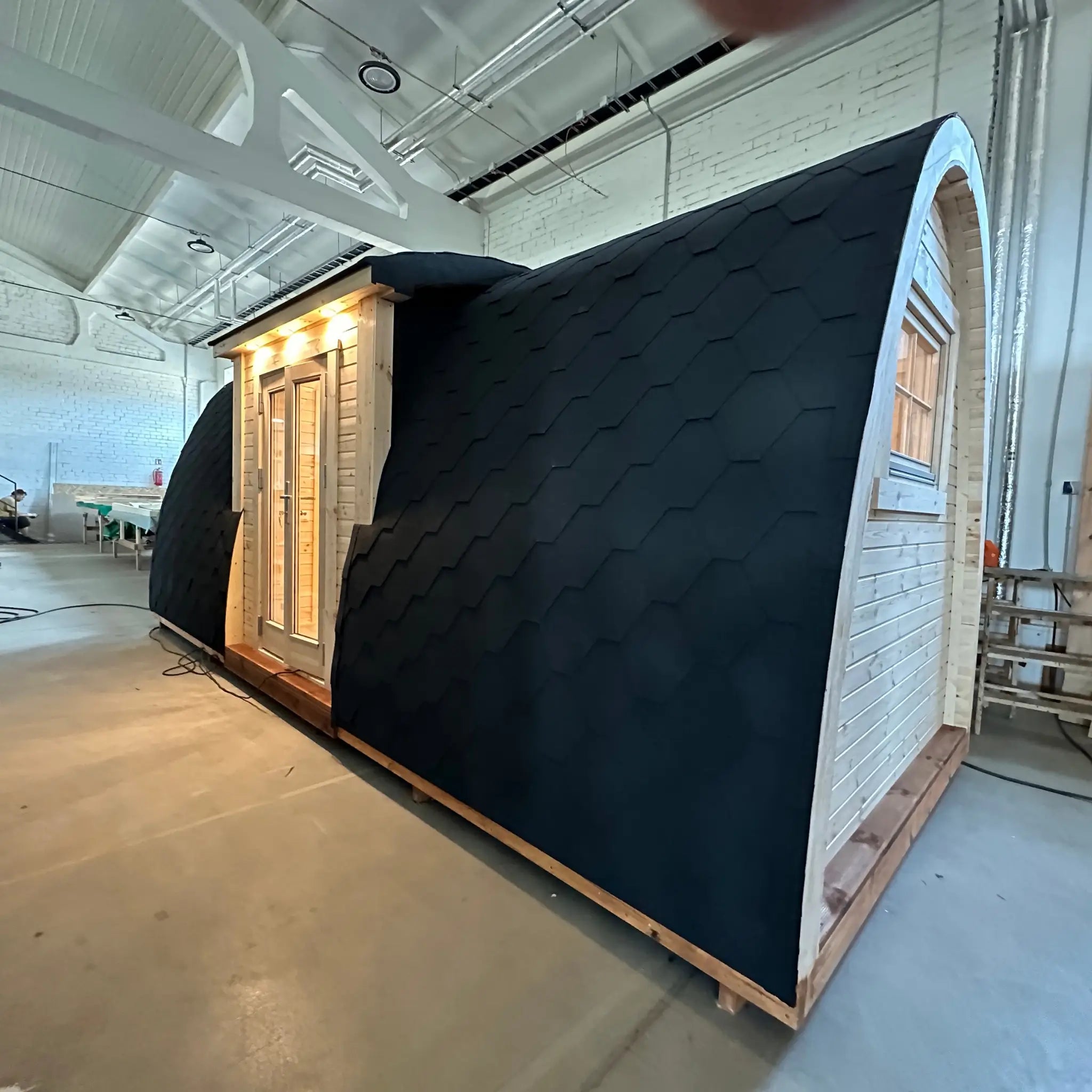 Angled side exterior view of the Hearthwood luxury pod showing black shingle cladding and timber base