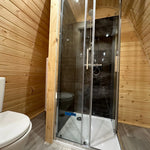 Interior bathroom of the Hearthwood glamping pod with shower enclosure, toilet, and timber wall finish