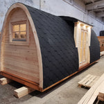 Left side exterior view of The Hearthwood Pod luxury glamping pod showing curved black shingle roof and timber base