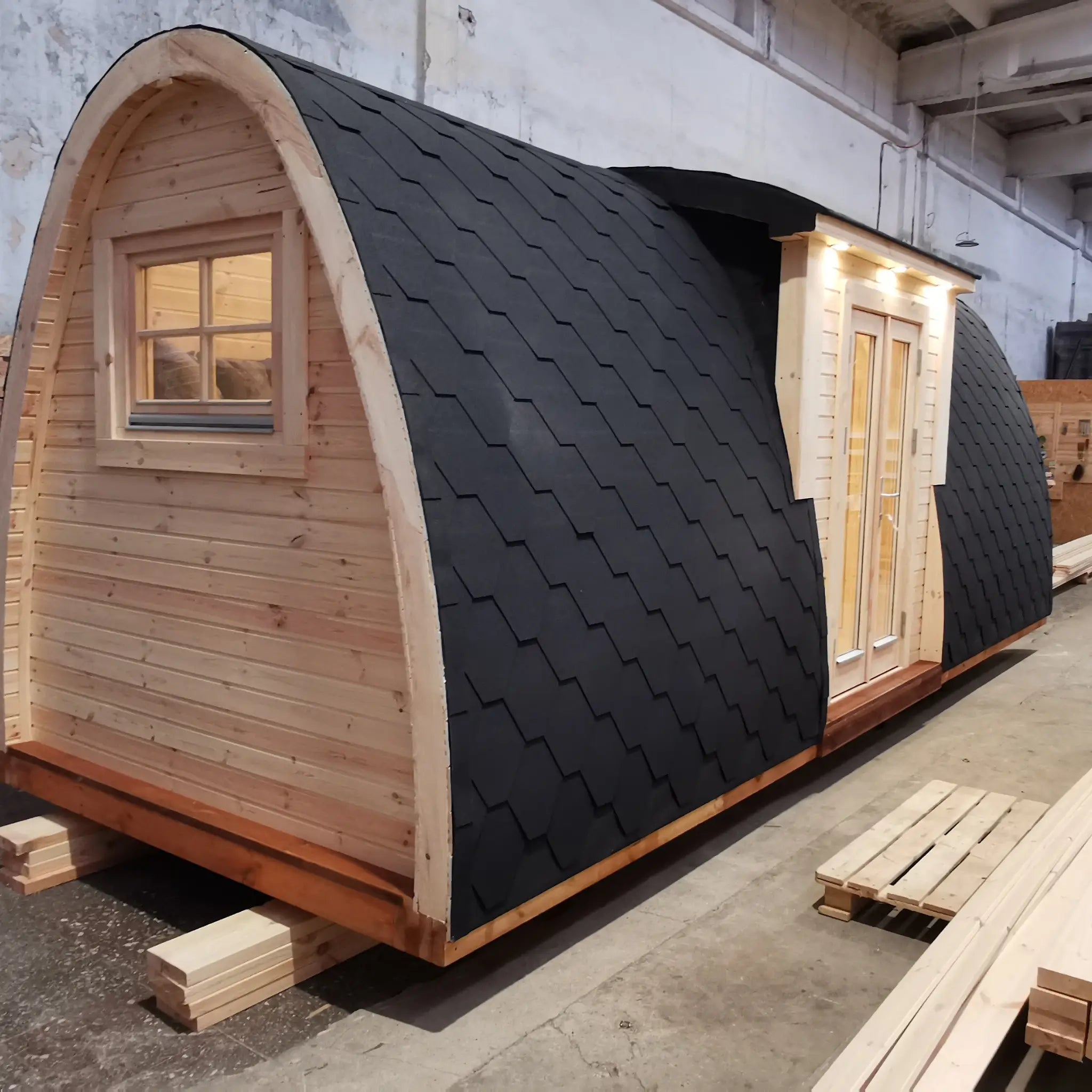 Left side exterior view of The Hearthwood Pod luxury glamping pod showing curved black shingle roof and timber base