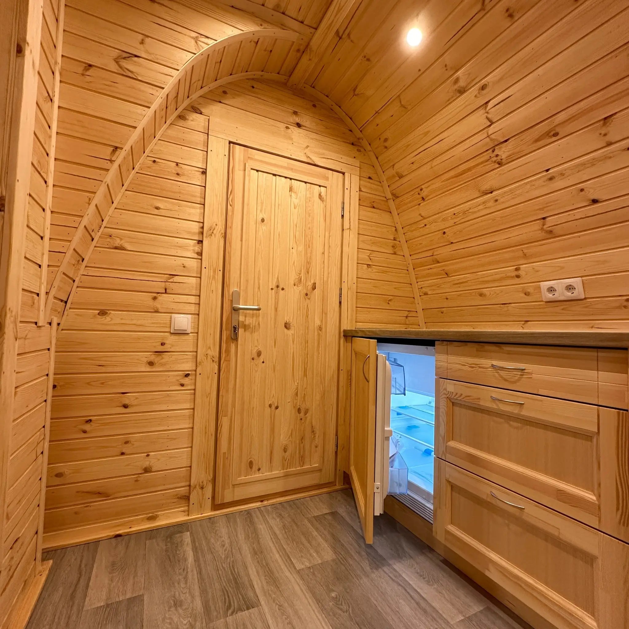 Compact kitchenette with built-in fridge and timber cabinetry inside The Hearthwood Pod luxury 6 person glamping pod