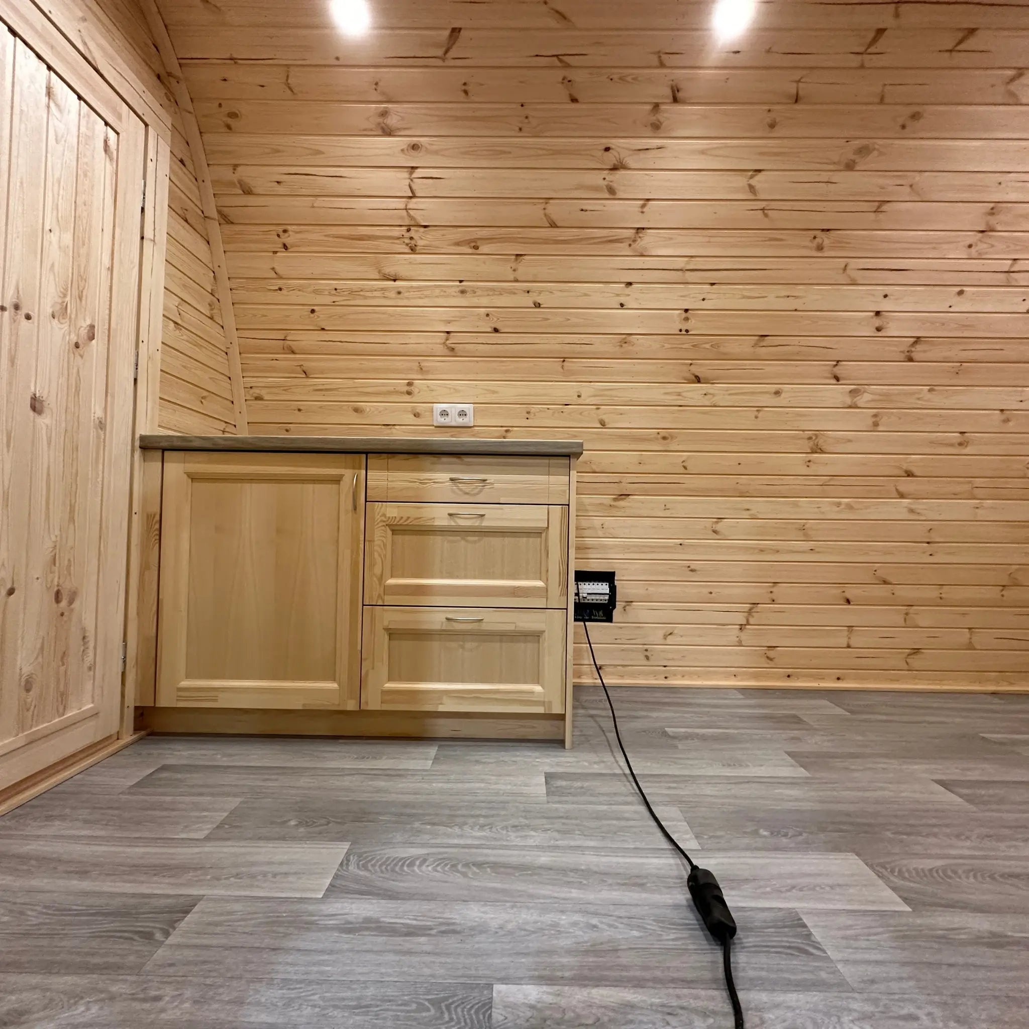 Open-plan living area with kitchenette and curved timber walls inside The Hearthwood Pod luxury 6 person glamping pod