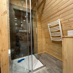Compact bathroom with shower enclosure and heated towel rail inside The Hearthwood Pod luxury glamping pod