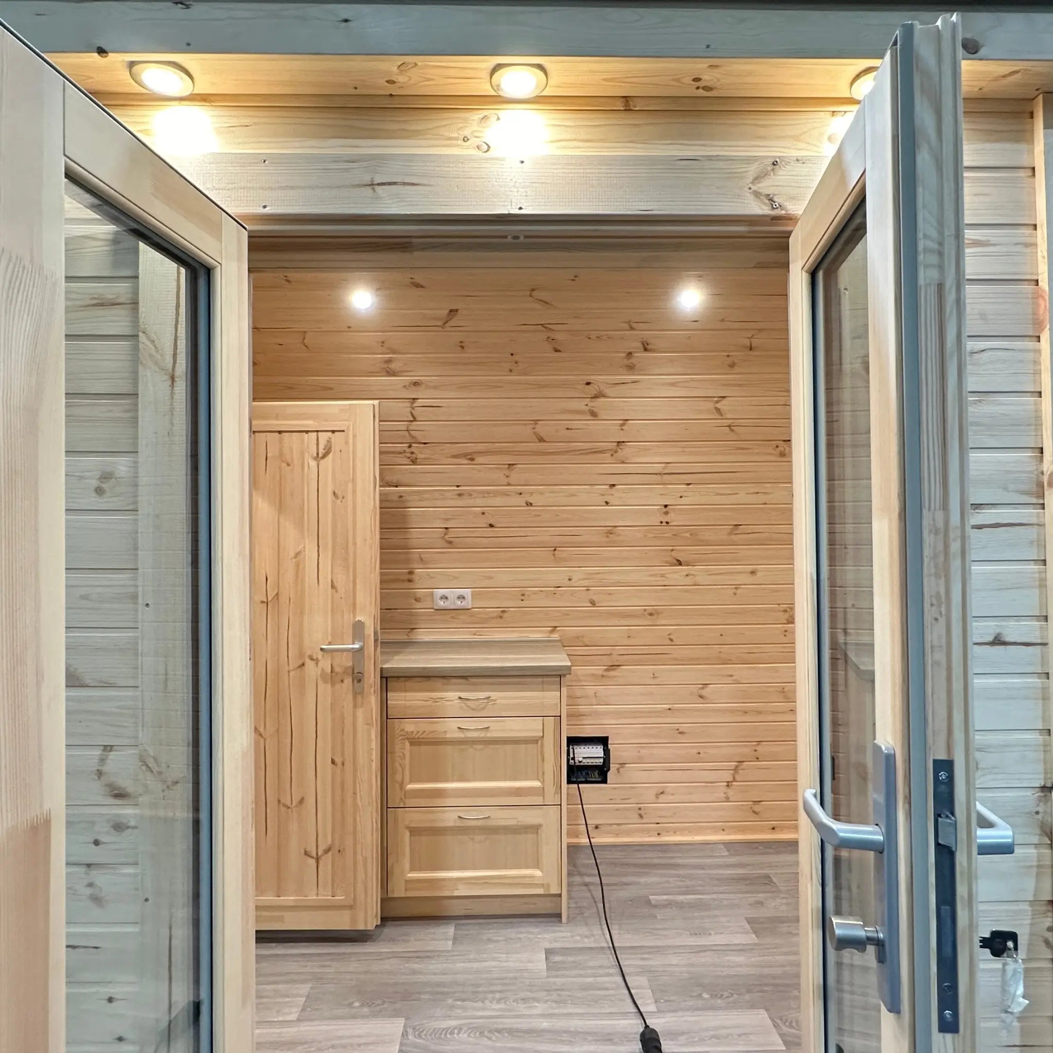 Interior view through entrance doors showing kitchenette and living space in The Hearthwood Pod luxury 6 person glamping pod