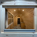 View into The Hearthwood Pod interior through an open window, highlighting the curved wooden ceiling and compact kitchenette area