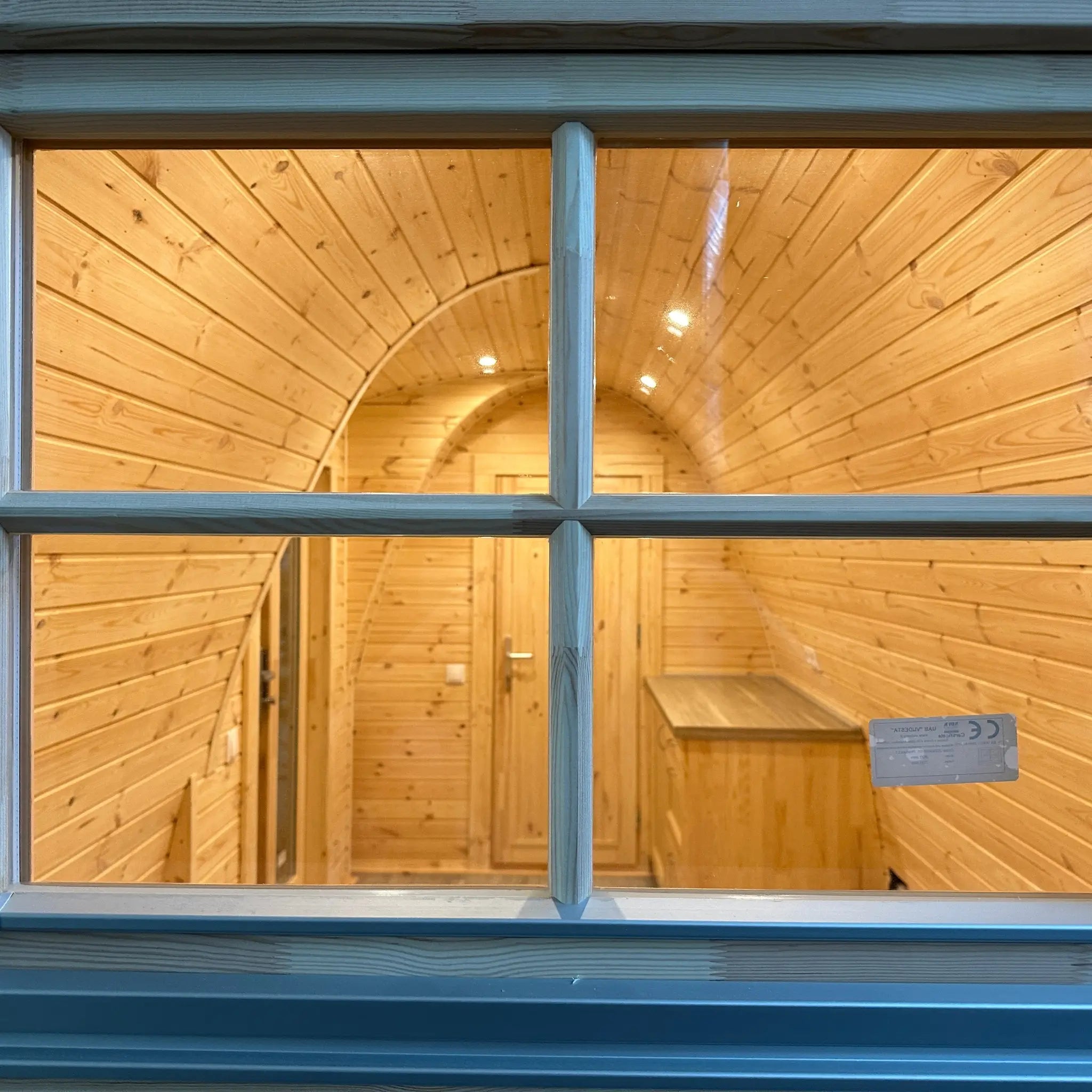 Close-up view through window into The Hearthwood Pod interior featuring timber-clad walls, recessed ceiling lights, and modern glamping layout