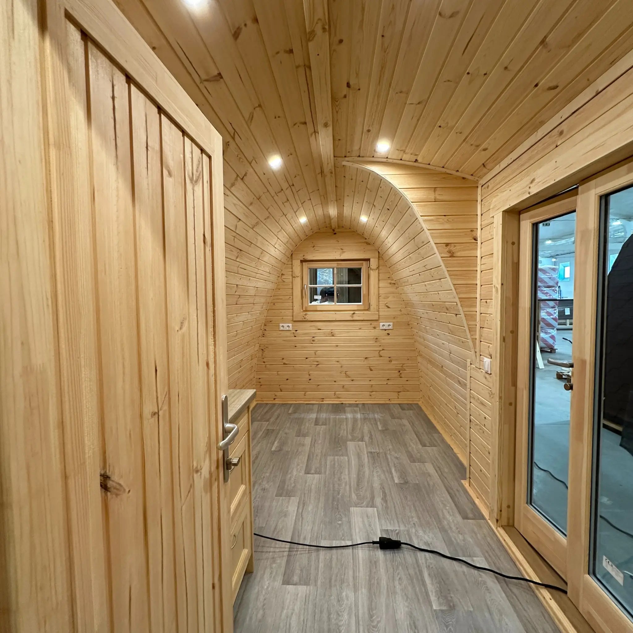 Interior perspective from bathroom area into the open living space of The Hearthwood Pod, showing curved architecture and natural wood finish