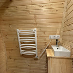 Compact glamping pod bathroom with electric towel radiator, timber wall cladding, and modern sink unit in The Hearthwood Pod