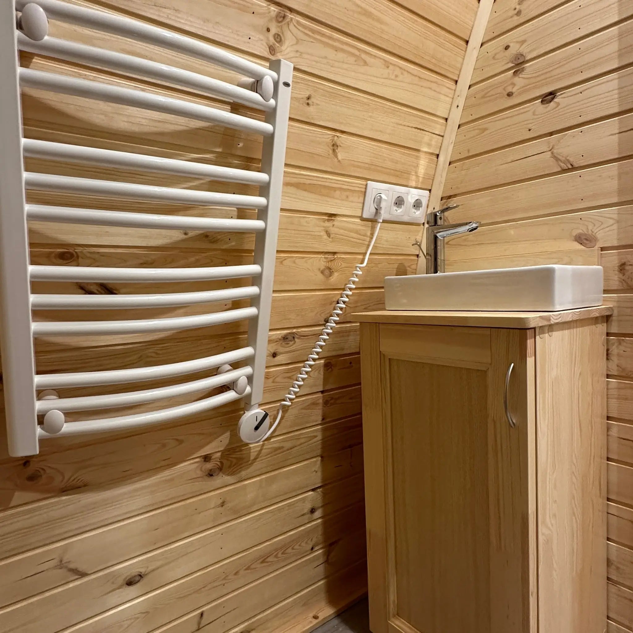 Bathroom close-up in The Hearthwood Pod featuring wall-mounted electric towel dryer and wooden vanity with ceramic wash basin