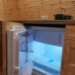 Built-in mini fridge inside luxury glamping pod kitchen with integrated wooden cabinetry