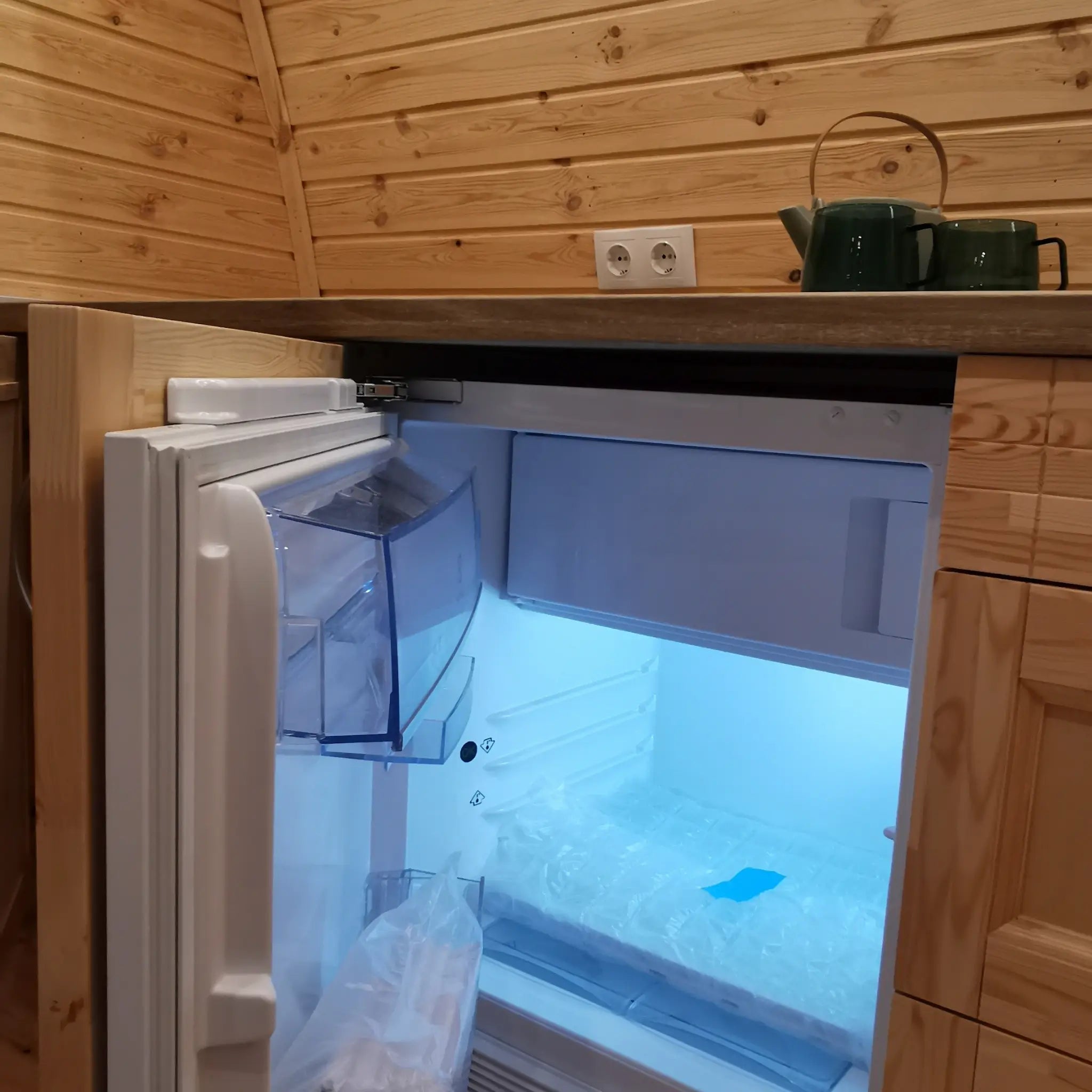Built-in mini fridge inside luxury glamping pod kitchen with integrated wooden cabinetry
