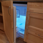 Close-up of open mini fridge in glamping pod kitchen with internal shelving and cool LED lighting