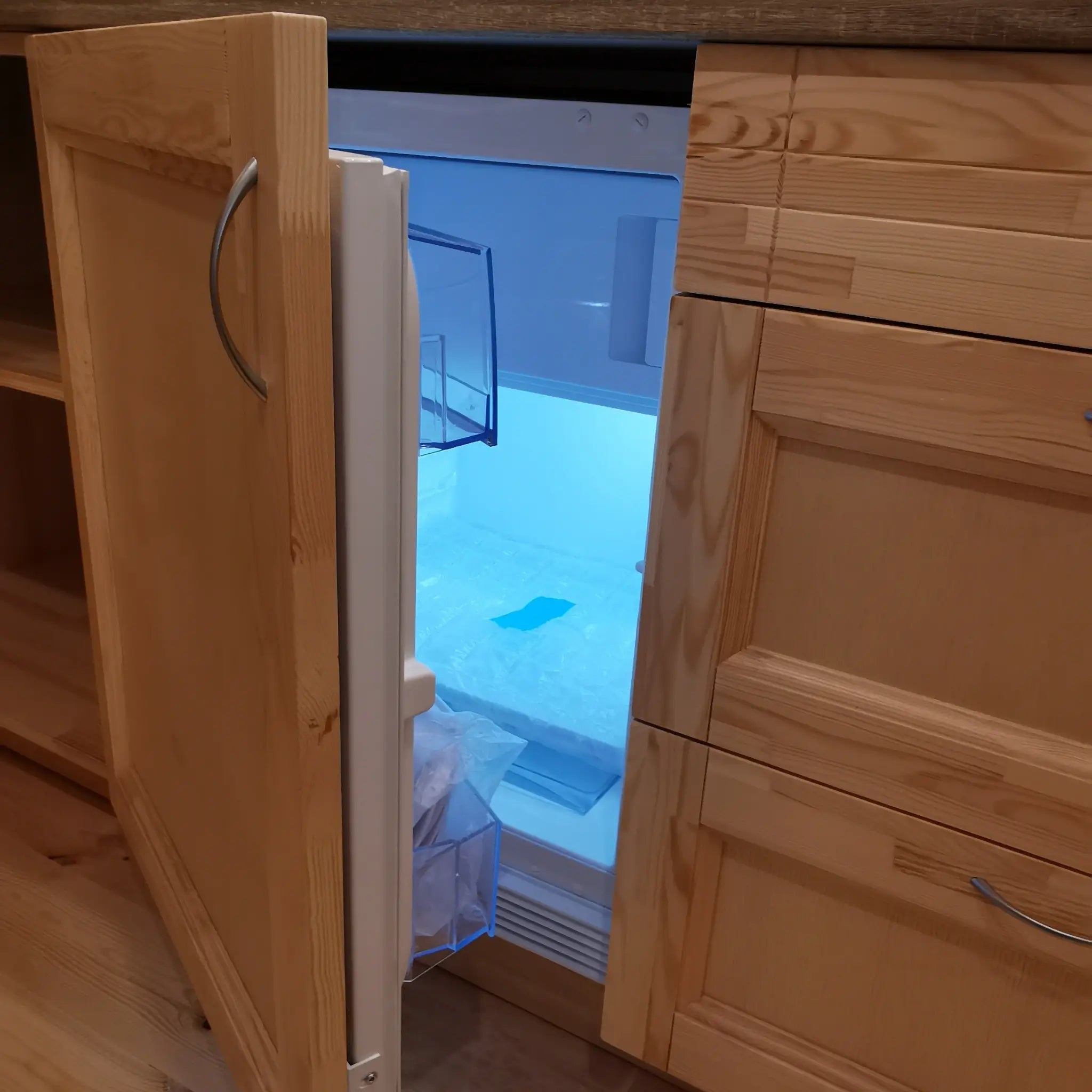 Close-up of open mini fridge in glamping pod kitchen with internal shelving and cool LED lighting