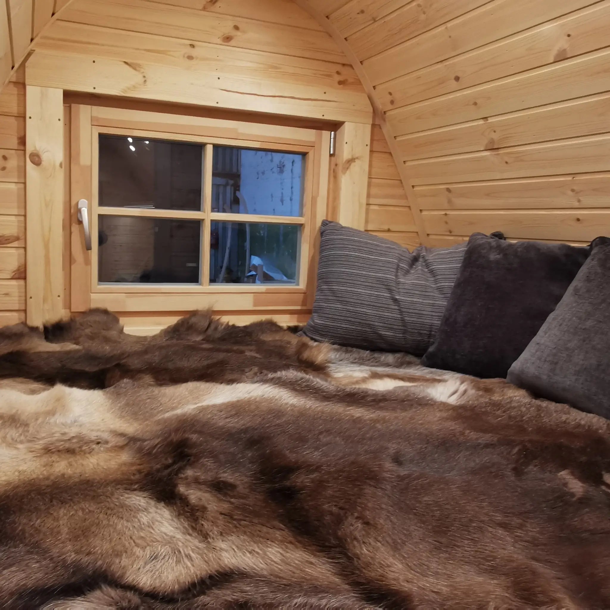 Top bunk sleeping area inside the Hearthwood Pod luxury 2 person glamping pod, featuring curved timber walls, cosy fur throw, and window for natural light.