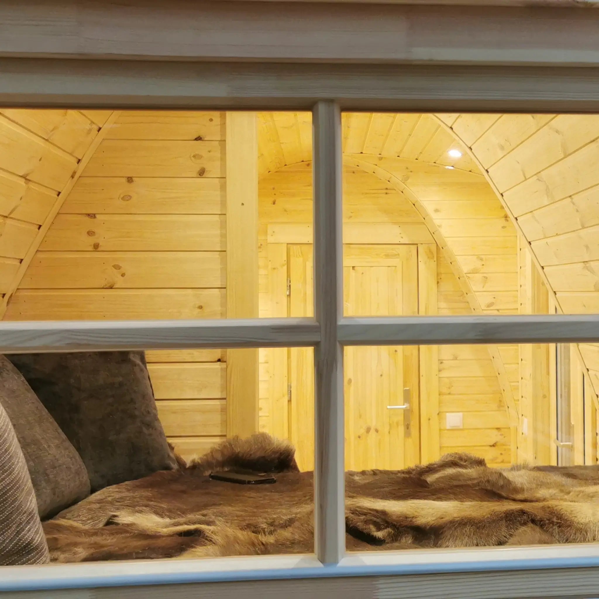 Interior view of the Hearthwood Pod luxury glamping pod seen through the window, highlighting the cosy sleeping space and natural timber finish.