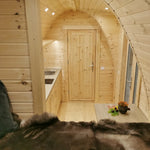 View from the bed towards the kitchenette and bathroom door inside the Hearthwood Pod luxury 2 person glamping pod, showing compact layout and timber-lined interior.
