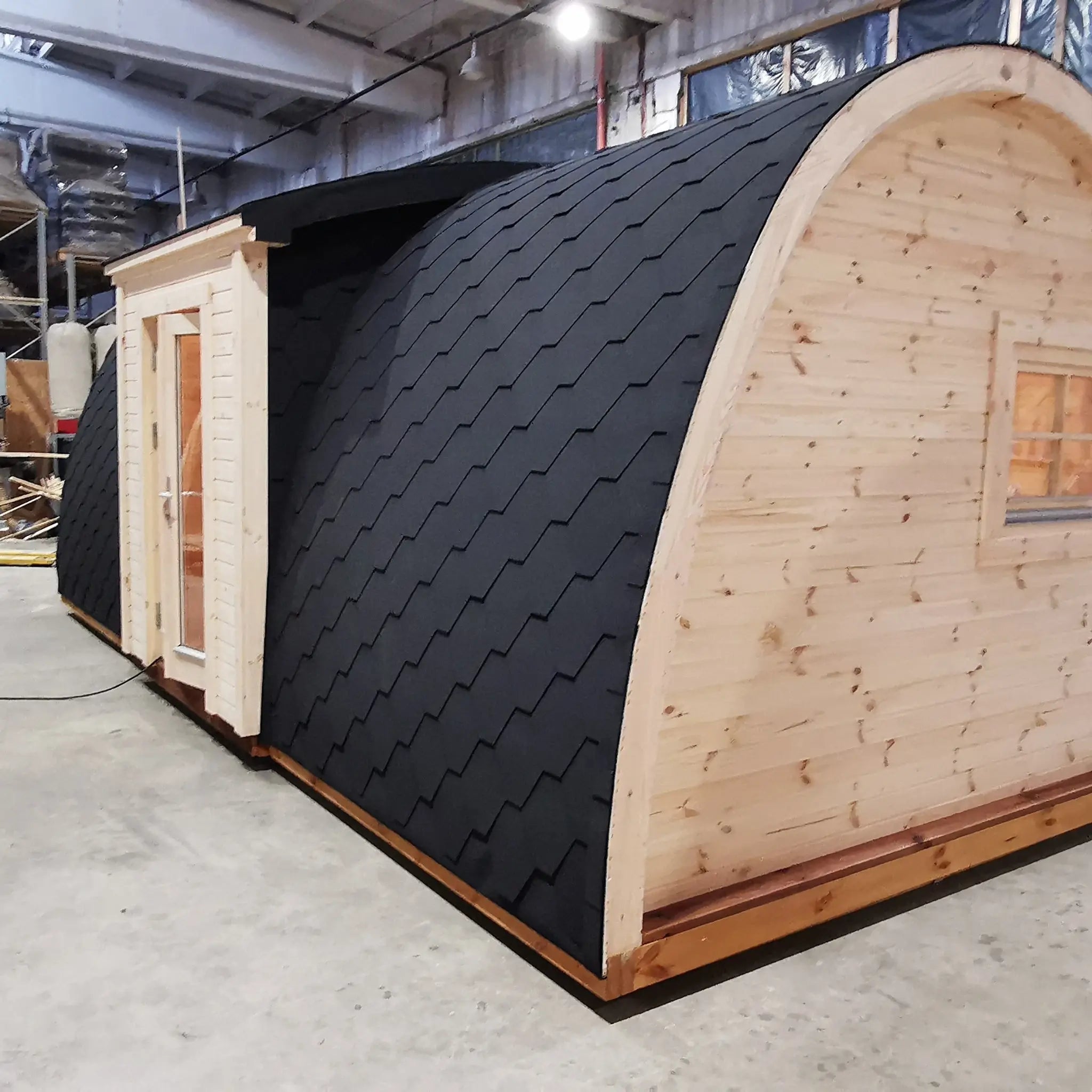 Exterior side view of The Hearthwood Pod luxury 6 person glamping pod with curved timber structure and insulated black shingle roof