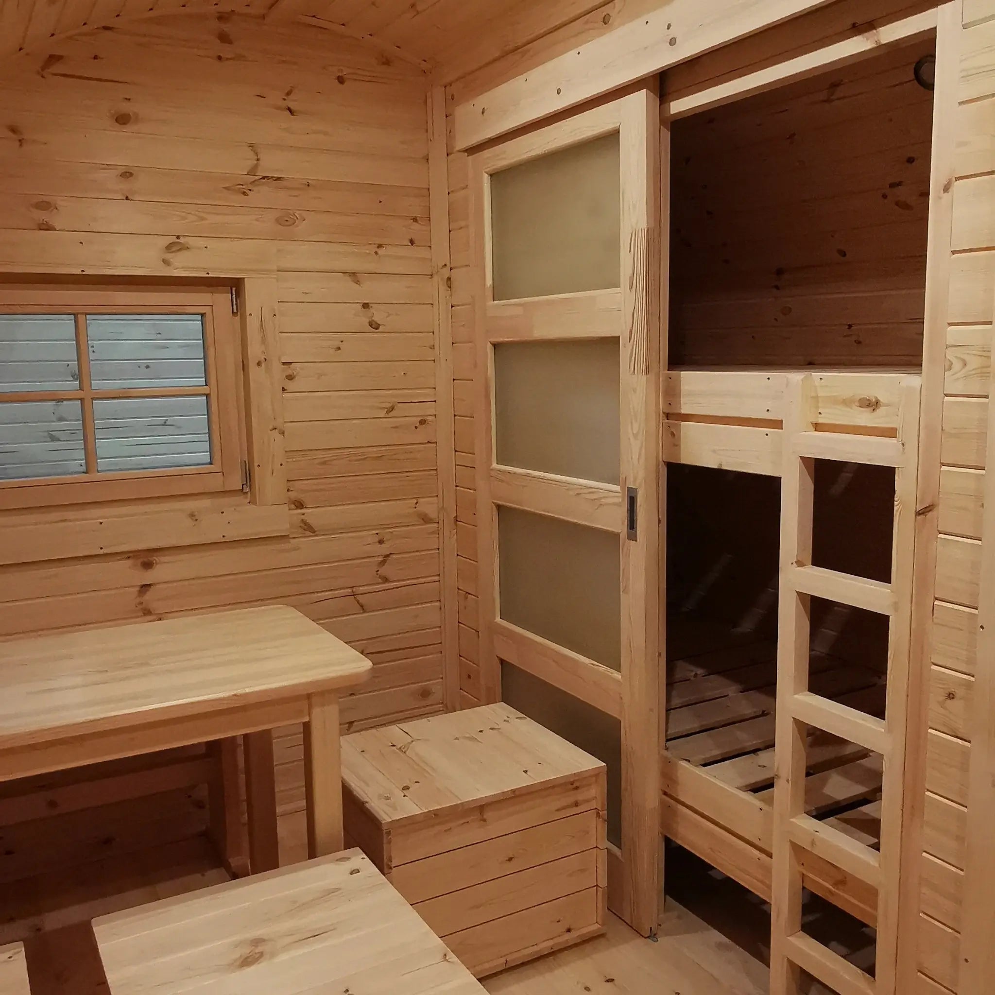 Dining area and bunk bed with sliding wooden door inside The Hearthwood Pod luxury 6 person glamping pod