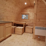 Timber-clad interior showing kitchenette, dining table, and wall-mounted radiator in the Hearthwood 6 person glamping pod