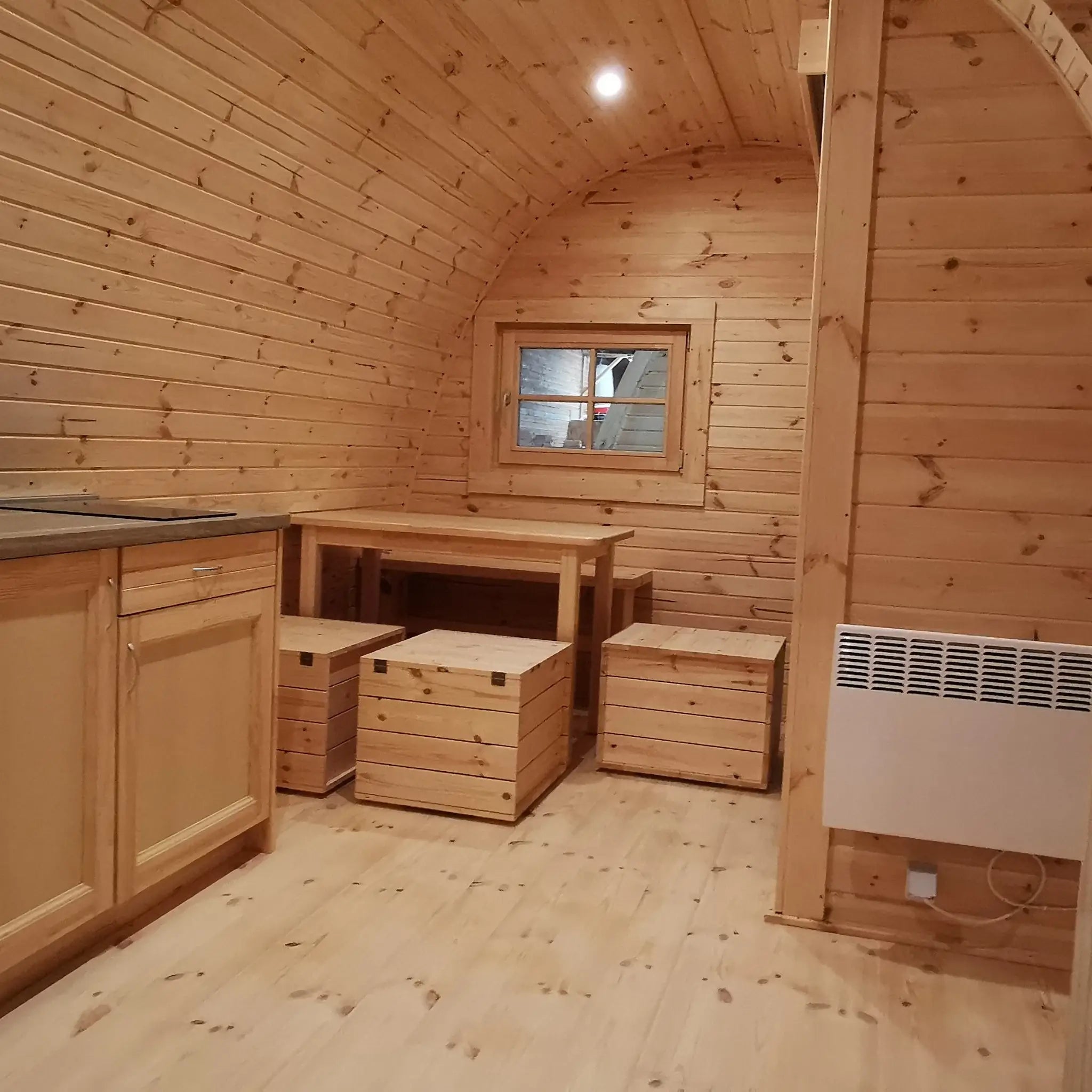 Timber-clad interior showing kitchenette, dining table, and wall-mounted radiator in the Hearthwood 6 person glamping pod