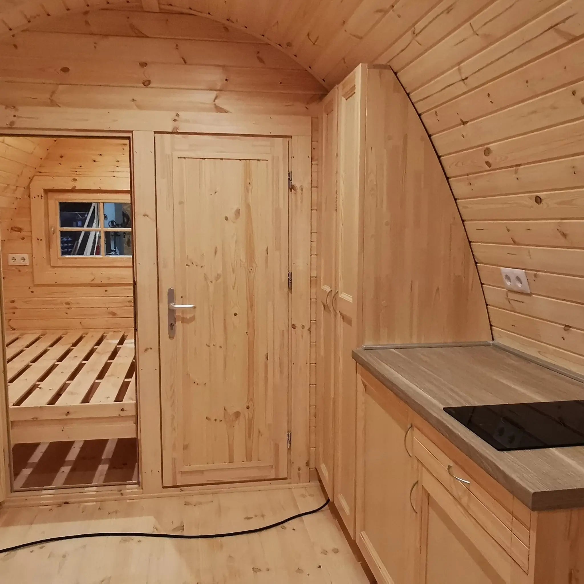 Curved timber interior featuring kitchenette, dining area, and compact radiator in the Hearthwood 6 berth glamping pod