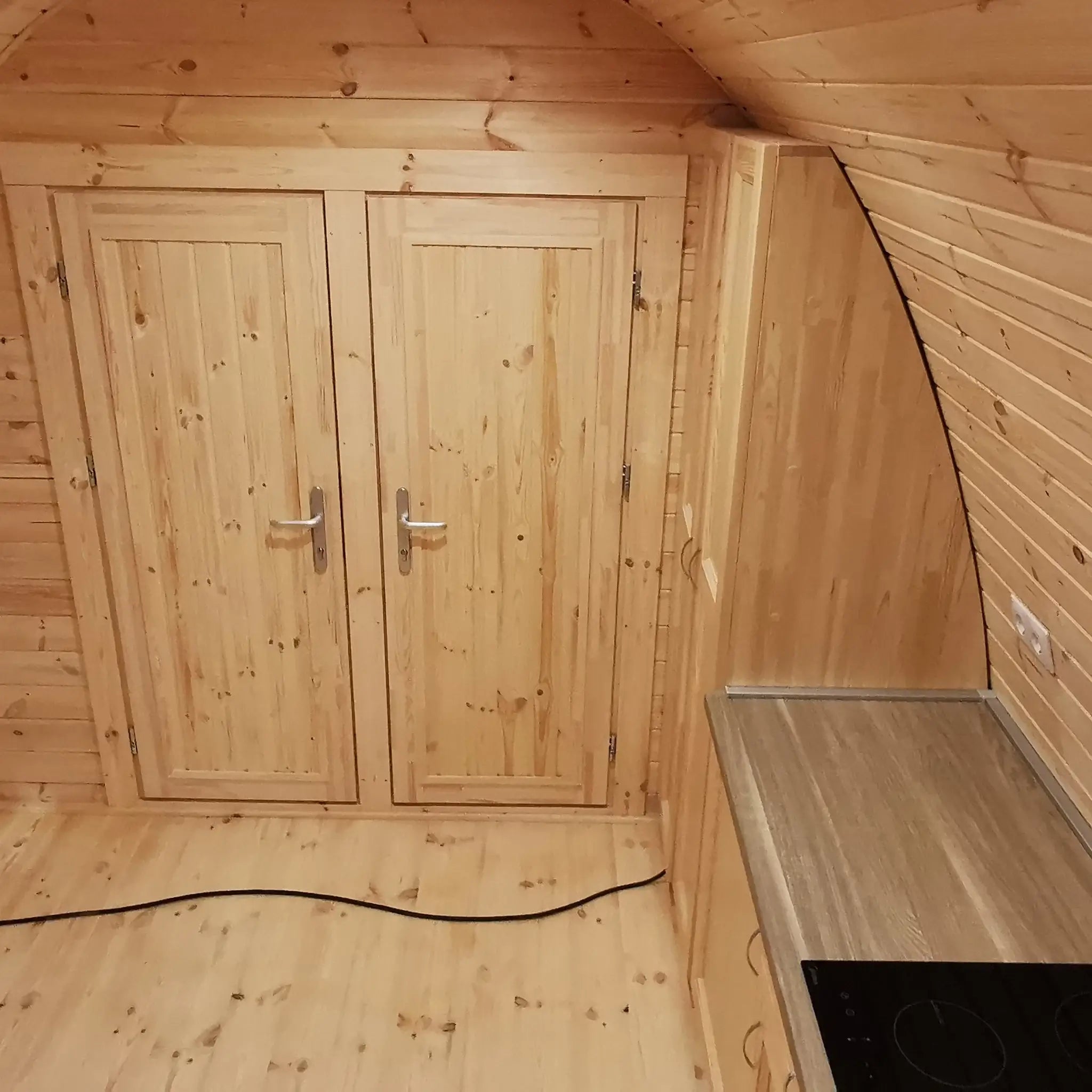 Timber-clad interior showing two bedroom doors and compact kitchen area in the Hearthwood Pod glamping accommodation