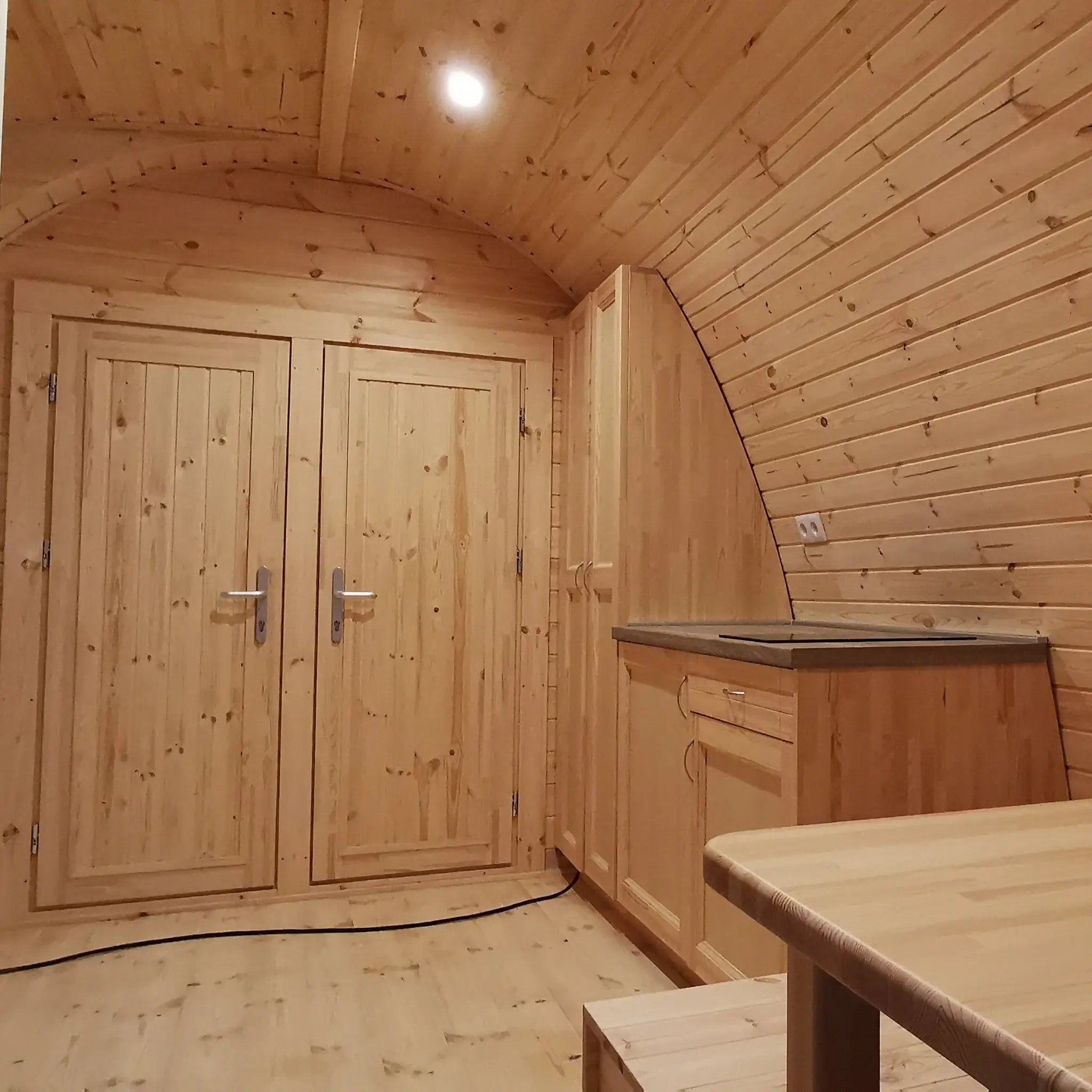 Interior dining space with twin bedroom doors and curved timber walls in the Hearthwood Pod glamping pod