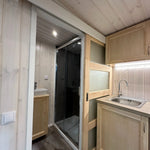 The Large GlampTainer container-style glamping unit – sleek kitchenette beside sliding door leading to bathroom with modern black-tiled shower