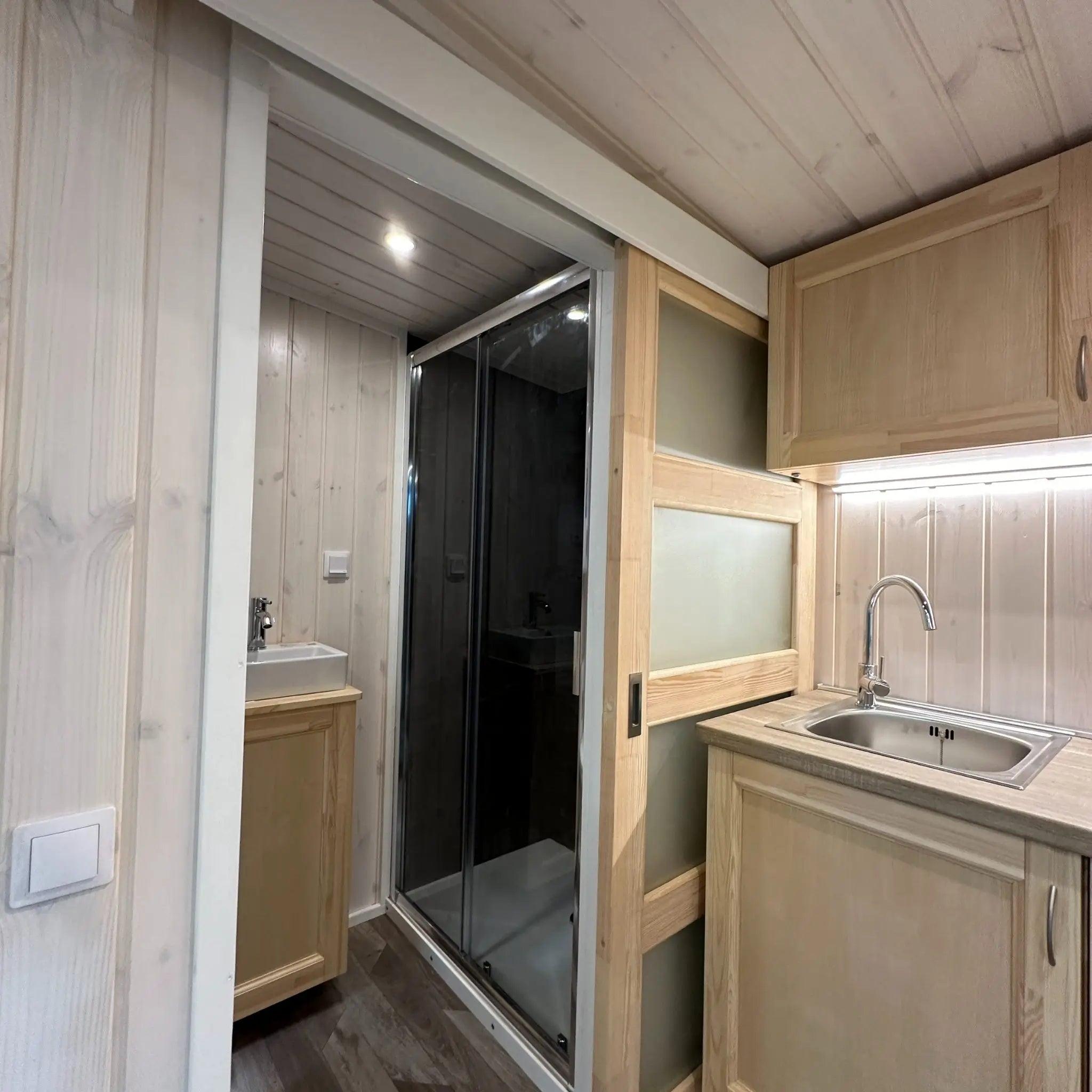 The Large GlampTainer container-style glamping unit – sleek kitchenette beside sliding door leading to bathroom with modern black-tiled shower