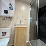 The Large GlampTainer container-style glamping unit – compact bathroom with toilet, basin, water heater and black-tiled standing shower