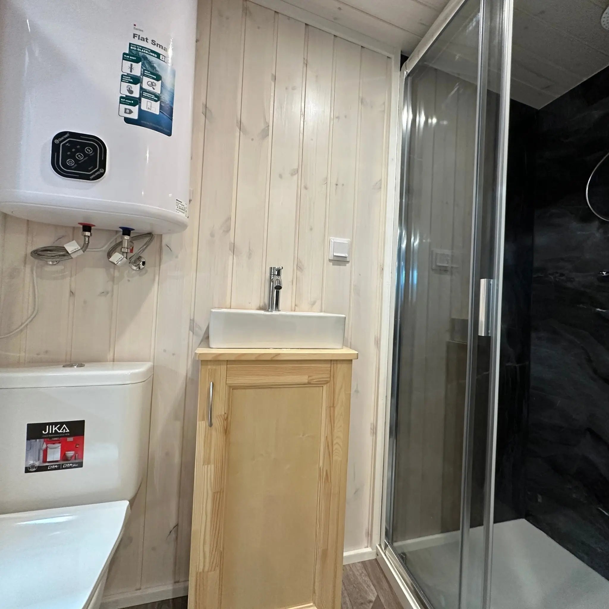 The Large GlampTainer container-style glamping unit – compact bathroom with toilet, basin, water heater and black-tiled standing shower