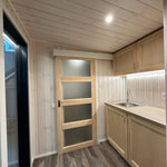 The Large GlampTainer container-style glamping unit – bright kitchenette with overhead cabinets next to closed frosted glass bathroom door