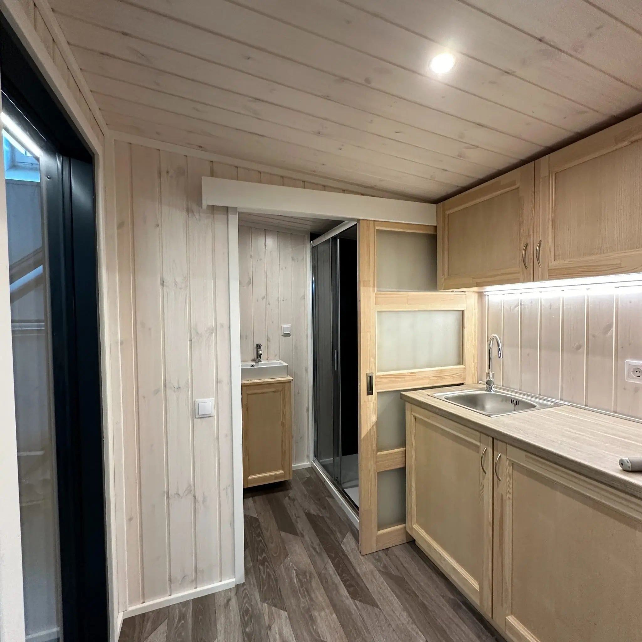 The Large GlampTainer container-style glamping unit – compact kitchenette with sink and LED lighting next to open bathroom entrance